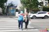 9月18日，在延吉市局子街北大市場西側的十字路口旁，大學志愿者劉書達頭戴志愿者標志帽、身穿藍馬甲、佩戴綬帶和袖標，手拿小紅旗，在路口維護交通秩序，引導行人通過斑馬線安全過馬路。
